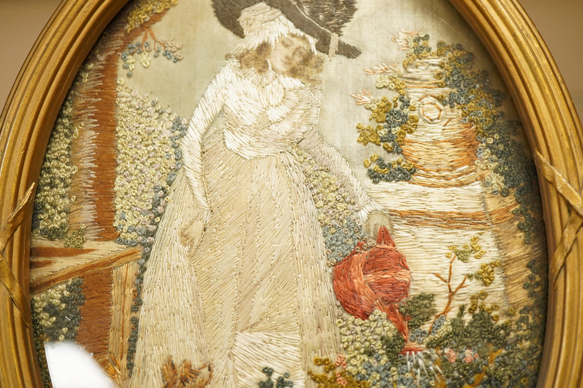A small oval gilt framed late 19th century silk polychrome embroidery of a lady watering her garden with her dog at her side, 19cm high. Condition - good.